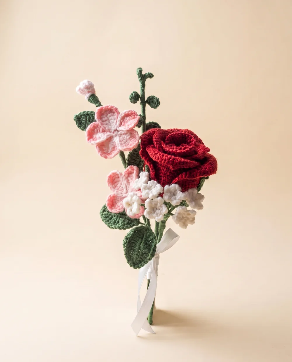 Crocheted bouquet with a red rose, pink and white flowers, presented on cream
